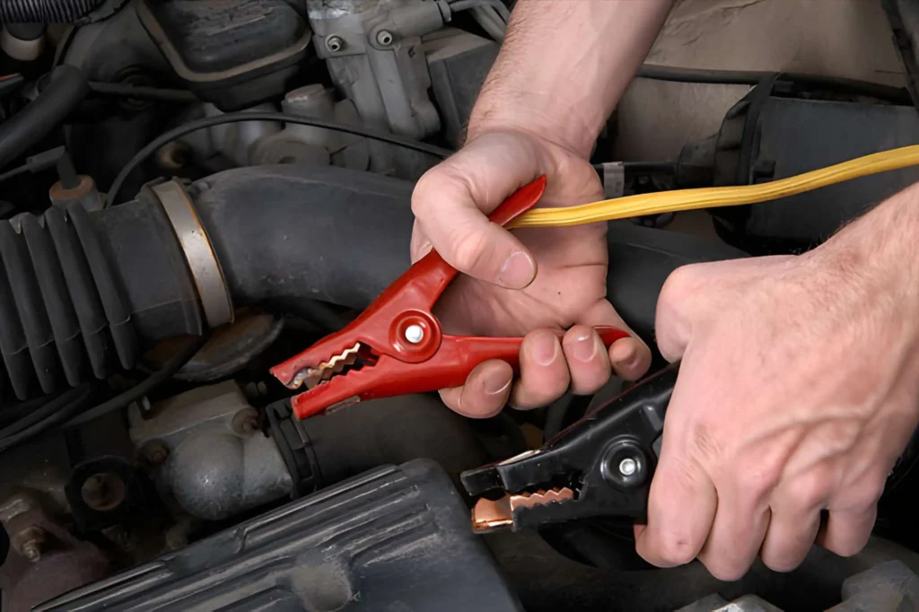 Mechanic holding red and black jumper cable clamps for a car jump start service by Car Jump Start Bros.