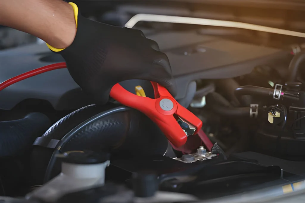 Professional mechanic connecting red and black jumper cables for a car jump start service in Radcliffe.