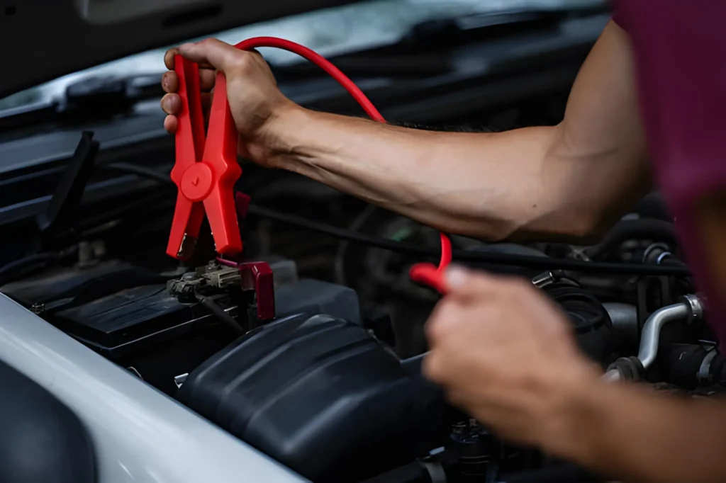 Professional mechanic using red booster cables to provide a car jump start service in Monton.